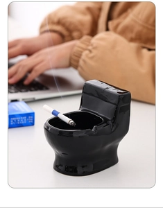 Detail of creative ceramic toilet shaped ashtray in black finish with a lit cigarette