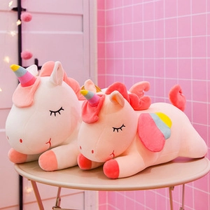 Close-up of two plush unicorn toys with rainbow horns on a beige table in cozy pink room