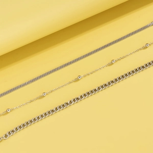 Detailed set of three silver snake bone, bead, and Cuban link chains on yellow background