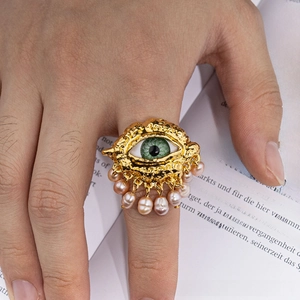 Close-up of a vintage golden Evil Eye ring with dangling light purple pearls worn on hand