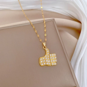 Elegant gold-plated thumbs up pendant necklace with pavé crystals on beige stand