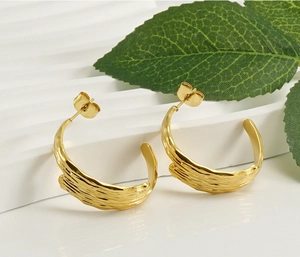 Macro detail of gold 18K plated C-hoop earrings featuring irregular lava texture surface