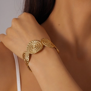 Détail des textures spirales dorées sur un bracelet métallique vintage porté au poignet