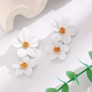 Detailed view of white flower stud earrings with gold centers on a clean marble surface