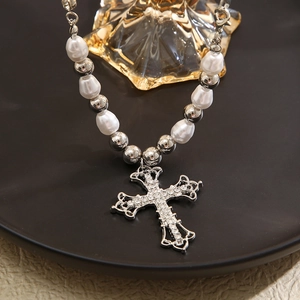 Detail of silver cross pendant with crystals and white pearl necklace on a tray