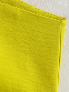 Dettaglio ravvicinato delle cuciture di precisione sul top in tessuto giallo brillante