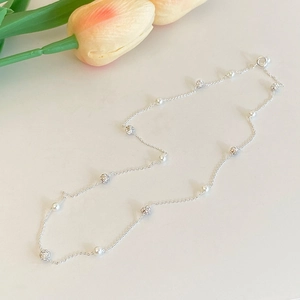 Gros plan du collier élégant en argent avec perles et sphères de zircon près de tulipes