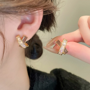 Detail of cross geometry gold-plated earrings with zircon stones and brown accents