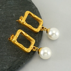 French style gold hammered rectangle earrings with white pearls on a stone background