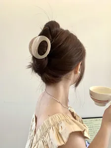Chic cream-colored oval hair claw clip shown styling a messy bun on dark brown hair