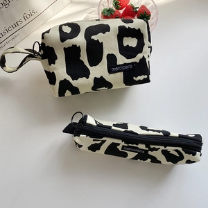 Detail of canvas pouches with cow print texture and black zipper rings on white desk