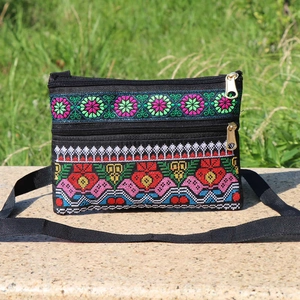 Detailed embroidery of colorful flowers on a black crossbody bag with double zippers