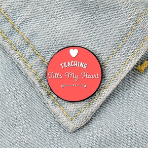 Red metal teaching brooch badge with TEACHING Fills My Heart text on denim background