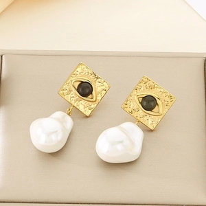Detail of gold square evil eye earrings with white baroque pearls on a jewelry tray