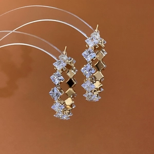 Detail of gold hoop earrings featuring clear square zircon stones on a brown background