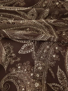 Détail du tissu en mousseline marron foncé avec motif paisley et textures plissées