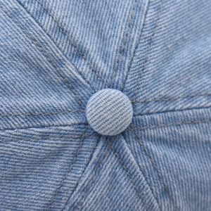 Macro view of the stitched crown and top button on a light blue denim baseball cap
