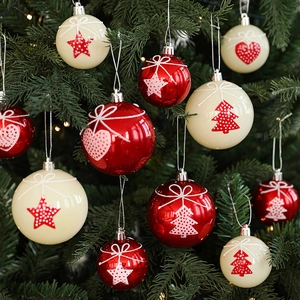 Red and cream Christmas balls with star heart patterns hanging on green pine branches