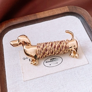 Macro detail of a golden dachshund dog brooch featuring woven colorful cord wrap texture