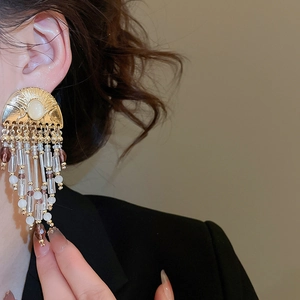 Close-up of vintage gold tassel earrings with cream stones and beaded fringe on a model