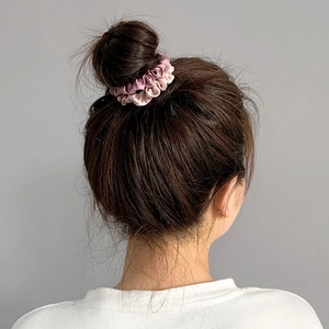 Detail view of pink and purple satin scrunchies worn on a bun hairstyle for styling