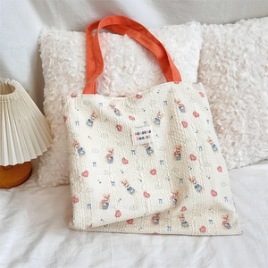 Detail of beige canvas tote bag with orange handles, featuring a cute bunny and heart print
