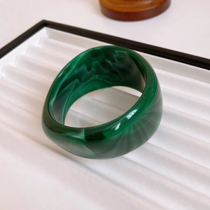 Close-up of a wide green marble texture bangle on a white minimalist jewelry tray