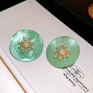 Détail macro de boucles d'oreilles fleurs vertes avec bordure dorée, perles et cristaux