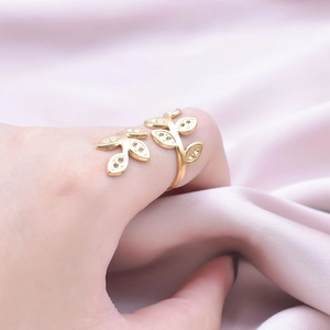 Detail of leaf design open ring in gold finish worn on hand over pink silk fabric