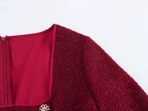 Gros plan du col en tweed bordeaux avec bouton fleur dorée et texture scintillante