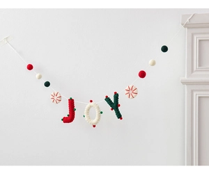 Close-up of JOY wool felt banner with colorful pompoms on white wall for Christmas decor