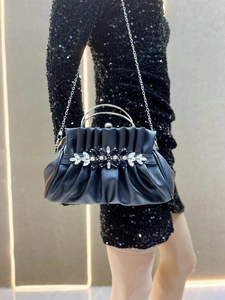 Detail of black pleated evening bag featuring a crystal floral buckle and silver handle