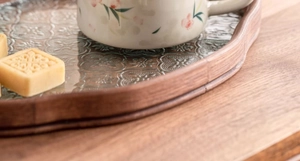 Close-up of a floral ceramic mug and pastries on a wooden tray with embossed glass base