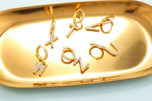 Detailed close-up of golden alphabet earrings set with zircons on a metal tray