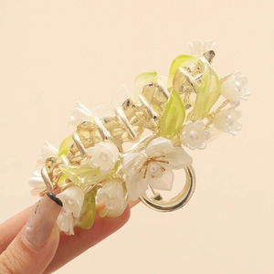Close-up of golden floral claw clip with white camellia and green leaves detail