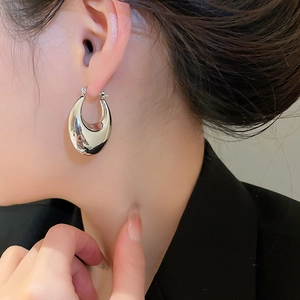 Close-up of chunky silver oval hoop earring with polished mirror finish on model