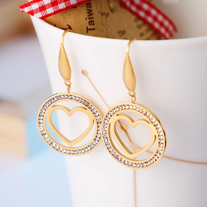 Golden heart drop earrings with zircon circle hanging on a white porcelain cup