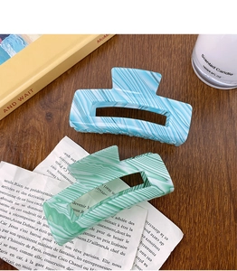 Close-up of blue and green marble pattern hair claws on a rustic wooden table
