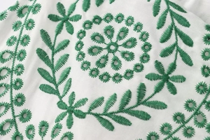 Nahaufnahme von weißem Baumwollstoff mit grüner Blumenstickerei und feiner Lochstickerei
