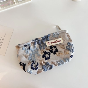 Detail of floral jacquard fabric texture on a compact blue and beige cosmetic pouch