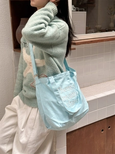 Detail view of light blue canvas tote bag with white embroidery on a female model