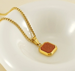Macro d'un pendentif en pierre de sable dorée sur une chaîne box dans un bol blanc