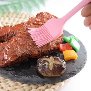 Pink silicone basting brush applying sauce to meat on a stone plate for baking