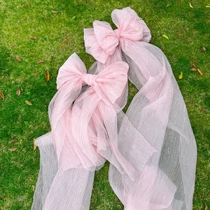 Detail of two large light pink pleated tulle bows placed on green grass outdoors