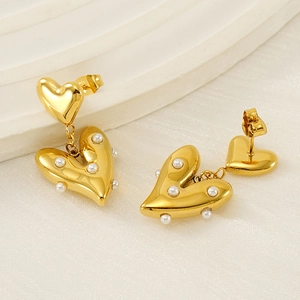 Elegant gold heart-shaped drop earrings with inlaid pearls on textured white fabric