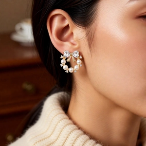 Detail of elegant bow earring with heart zirconia and small white pearls on a model