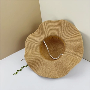 Détail d'un chapeau de soleil en paille à larges bords ondulés avec sangle élastique vent