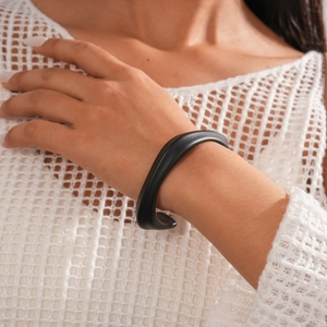 Detail of matte black irregular geometric cuff bangle on model with contrast background