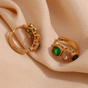 Detailed macro of gold-plated hoop earrings featuring inlaid green and blue gemstones