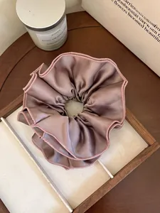 Close-up of premium dusty rose satin scrunchie with elegant wavy edges on a wooden tray